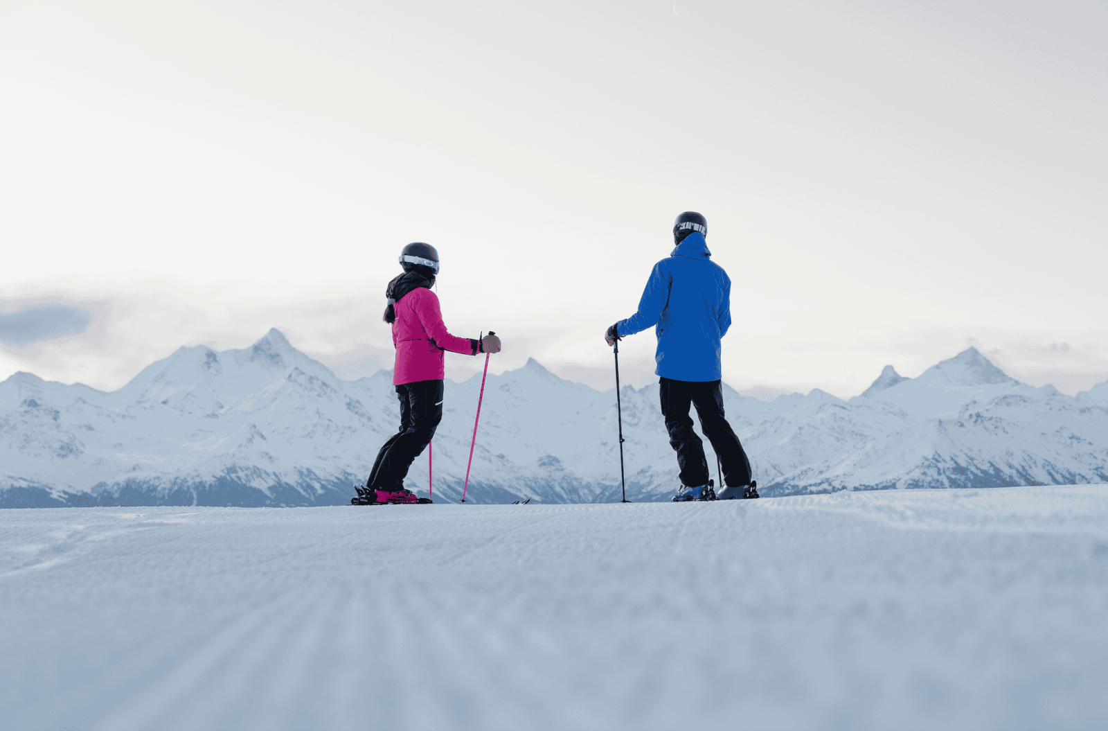 Two skiers enjoying the snowy slopes of Crans-Montana, Switzerland, with panoramic views of the Swiss Alps.